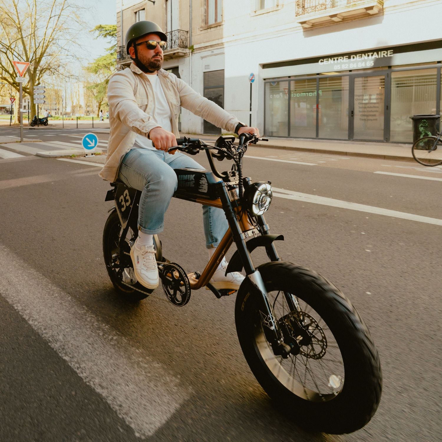 Fatbike électrique biplace City XL Unikride sur route urbaine, avec phare rond, pneus larges et selle biplace.