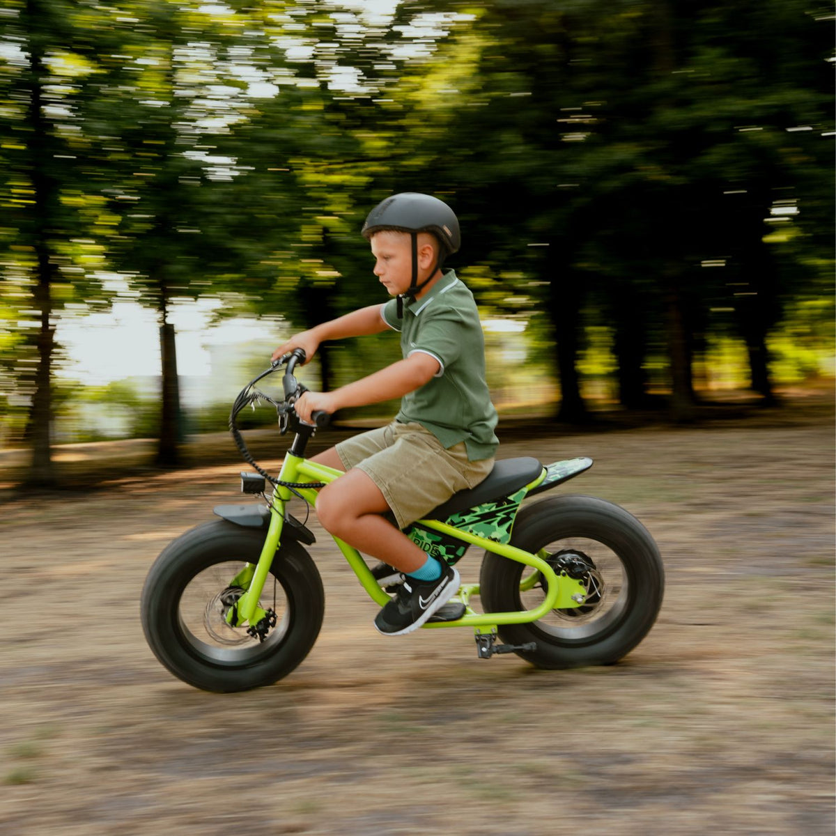 Enfant casqué roulant vite sur la draisienne électrique Fat Fun verte, effet de mouvement sur chemin forestier