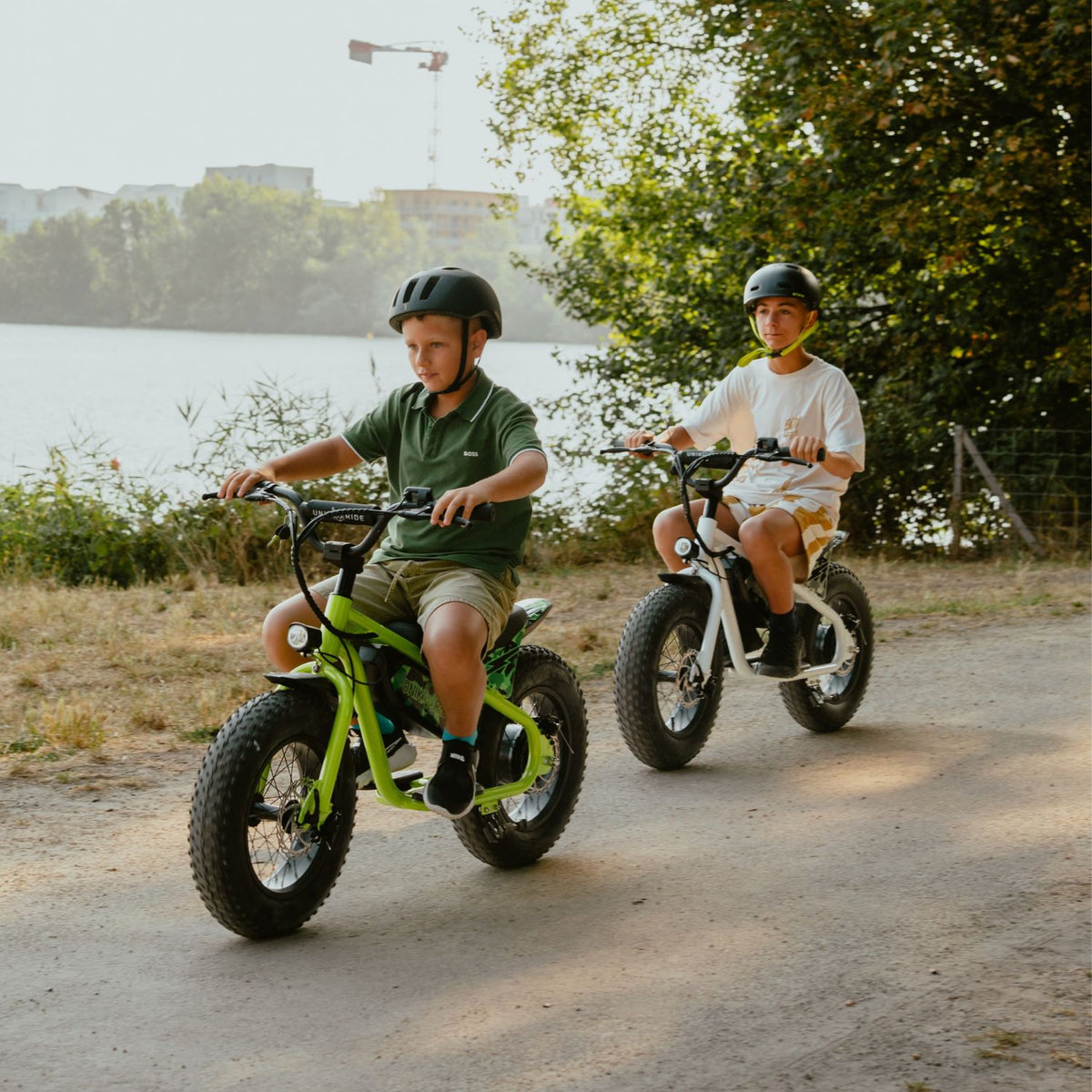 Deux enfants casqués sur des draisiennes électriques Fat Fun 16 pouces roulant au bord d'un lac