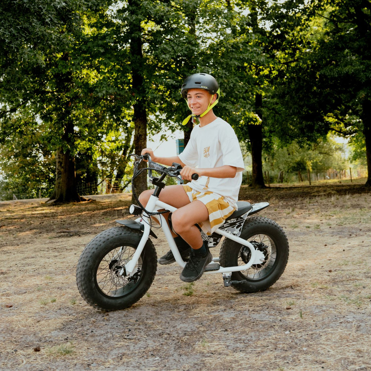 Enfant casqué sur la draisienne électrique Fat Fun 16 pouces blanche, pneus fat bike sur chemin de forêt